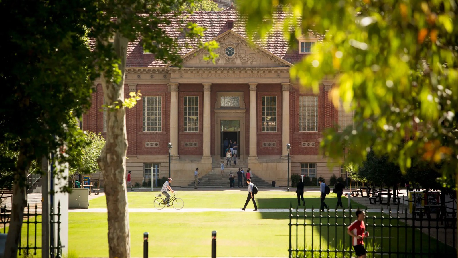 澳洲大學歷史圖書館建築與草坪，學生騎單車及步行經過