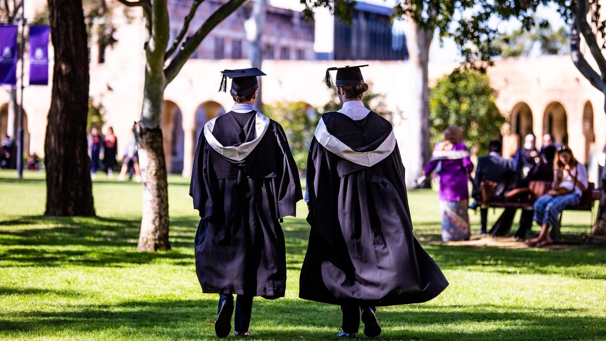 兩位穿學袍及方帽的碩士畢業生走過大學草坪